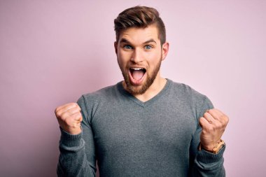 Sarışın, sakallı ve mavi gözlü genç bir adam, sıradan bir süveter giyip kollarını kaldırıp, gözleri açık bir şekilde başarıyı kutluyor. Kazanan konsept.