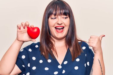 Kalbini tutan genç ve iri bir kadın baş parmağını yana kaldırmış, ağzı açık gülümsüyor. 