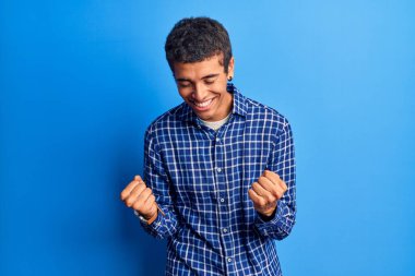 Genç Afrikalı Amerikalı sıradan kıyafetler giyen çok mutlu ve heyecanlı kolları havada, gülümseyen ve başarı için çığlık atan kazanan bir jest yapıyor. kutlama konsepti. 