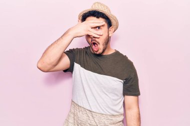 Gündelik kıyafetler giyen genç İspanyol adam şok içinde yüzünü ve gözlerini eliyle kapatıyor, parmaklarından korkuyla bakıyor. 