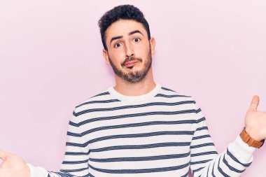 Sıradan kıyafetler giyen, elleri ve kolları havada, kafası karışmış genç İspanyol bir adam. şüphe kavramı. 