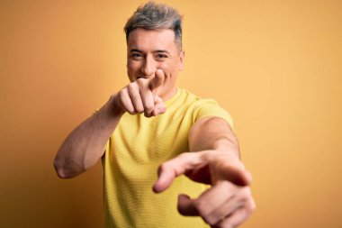 Sarıya boyanmış sarı tişörtlü, genç ve modern adam seni ve kamerayı parmaklarıyla göstererek mutlu ve mutlu bir şekilde gülümsüyor.