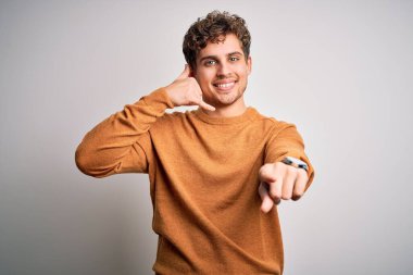 Sarışın, kıvırcık saçlı, beyaz arka planda rahat süveter giyen, gülümseyen, telefonda konuşan ve seni işaret eden genç, yakışıklı bir adam. Ara beni..