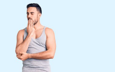 Mayo ve kolsuz tişört giyen genç yakışıklı adam ağzıyla esnemekten sıkılmış. Huzursuz ve uykulu.. 