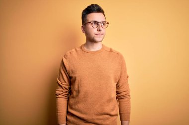 Genç, beyaz, gözlüklü ve sarı arka planda sıradan bir süveter giyen yakışıklı bir adam. Gülümsüyor ve başka tarafa bakıyor..