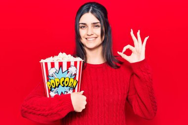 Genç ve güzel bir kız patlamış mısır yiyor. Parmaklarıyla imza atıyor, gülümsüyor. Mükemmel bir sembol. 