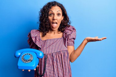 Orta yaşlı, güzel bir kadın elinde klasik bir telefonla başarıyı kutluyor mutlu bir gülümsemeyle ve kazanan bir ifadeyle elini kaldırarak. 