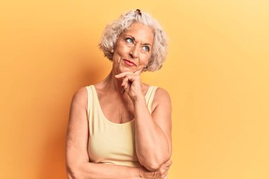 Yaşlı, gri saçlı, sıradan kıyafetler giyen, eli çenesinde soru soran, düşünceli bir kadın. Gülümseyen ve düşünceli bir yüz. şüphe kavramı. 