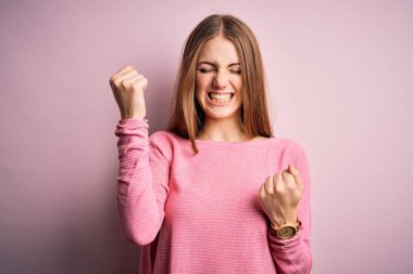 Genç, güzel, kızıl saçlı bir kadın izole edilmiş pembe arka plan üzerine gündelik süveter giyip kolları açık ve gözleri kapalı bir şekilde başarıyı kutluyor. Kazanan konsept.