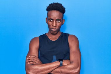 Afro-Amerikalı genç bir adam spor kıyafetleri giyiyor. Şüpheci ve gergin. Yüzünde çapraz kollarla onaylamayan bir ifade var. negatif kişi. 