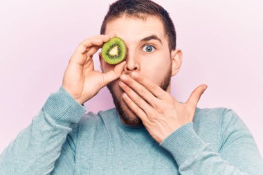 Genç yakışıklı bir adam, bir dilim kiviyi gözünün üzerinde tutuyor ağızlarını eliyle kapatıyor, şok geçiriyor ve hata yapmaktan korkuyor. şaşırmış ifade 