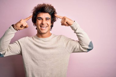 İzole edilmiş pembe arka plan üzerinde dikilmiş tişört giyen genç yakışıklı adam iki eliyle başını gösteren gülümseme, harika bir fikir ya da düşünce, iyi bir hafıza