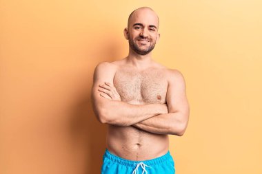 Mayosuz, mutlu yüzlü, kollarını kavuşturup kameraya bakan genç ve kel bir adam. pozitif kişi. 