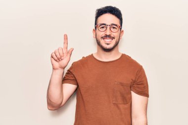 Bir fikir veya soruyla gülümseyen gündelik kıyafetler giyen genç İspanyol adam, bir numara, mutlu bir yüzle işaret ediyor. 