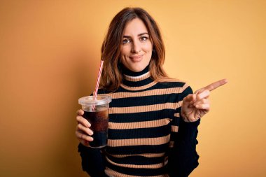 Genç, güzel, esmer bir kadın kola ile bardakta içki içiyor. Saman kullanarak mutlu bir şekilde elini ve parmağını kenarı işaret ediyor.