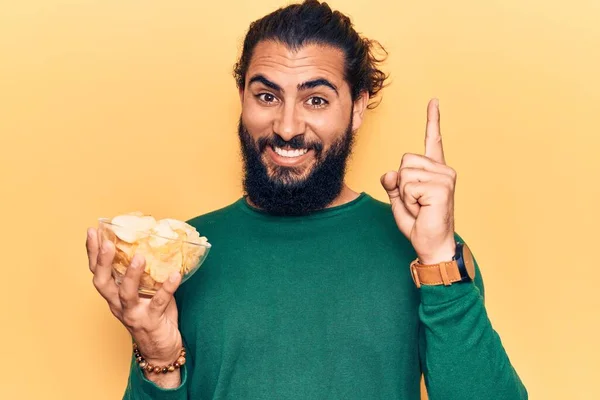 アイデアや質問と笑顔でポテトチップスを保持若いアラブ男幸せな顔を指差す指 ナンバーワン — ストック写真