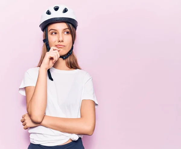 Young beautiful girl wearing bike helmet thinking concentrated about doubt with finger on chin and looking up wondering