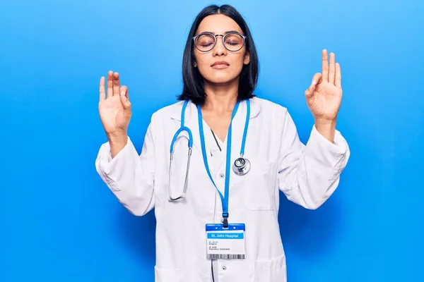 Young beautiful latin woman wearing doctor stethoscope and id card relax and smiling with eyes closed doing meditation gesture with fingers. yoga concept.