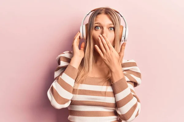 Młoda Blondynka Słuchająca Muzyki Pomocą Słuchawek Zakrywających Usta Ręką Zszokowana — Zdjęcie stockowe