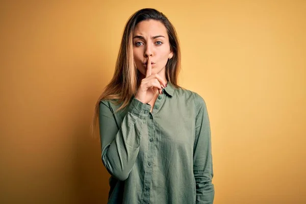 唇に指で静かにするように求める黄色の背景に緑色のシャツを着て青い目を持つ若い美しいブロンドの女性 沈黙と秘密の概念 — ストック写真