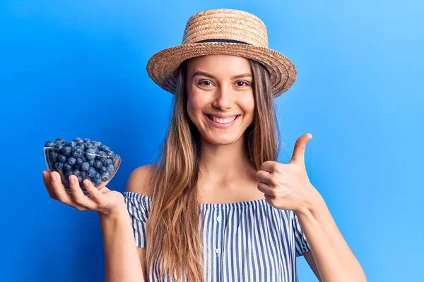 모자를 소녀가 블루베리 열매가 그릇을 행복하고 긍정적 미소를 있습니다 엄지손가락은 — 스톡 사진