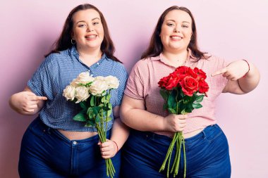 Çiçek tutan genç ve cüsseli ikizler mutlu bir şekilde elleri ve parmaklarıyla işaret ediyorlar. 