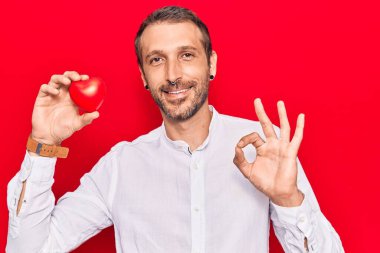 Kalbi tutan yakışıklı genç adam parmaklarıyla imza atıyor, gülümsüyor mükemmel bir sembol. 