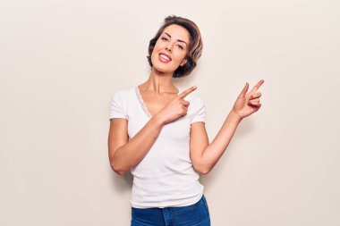 Genç, güzel bir kadın, günlük kıyafetler giyip gülümsüyor ve kameraya bakıyor. İki eliyle ve parmaklarıyla kenarı işaret ediyor.. 