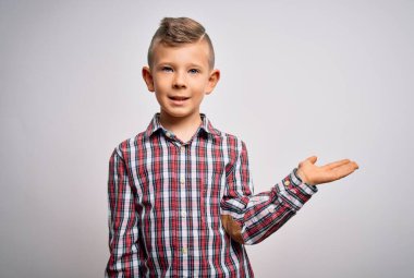 Mavi gözlü, zarif gömlekli, izole edilmiş arka planda duran neşeli bir şekilde gülümseyen ve avuç içi kameraya bakan küçük beyaz çocuk..