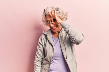 Kıdemli gri saçlı kadın, günlük spor kıyafetleri giyiyor, gülümsüyor ve gülümsüyor. 