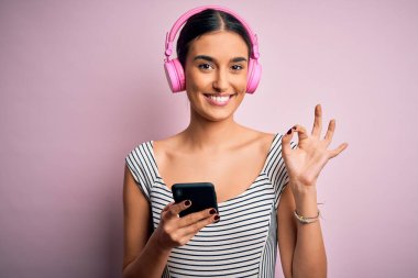 Genç, güzel esmer kadın müzik dinliyor kulaklık ve akıllı telefon kullanıyor. Parmaklarıyla imza atıyor. Mükemmel bir sembol.