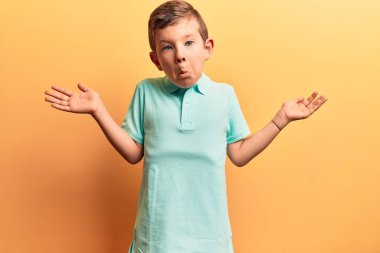 Sıradan kıyafetler giyen sevimli sarışın çocuk, habersiz ve kolları açık, hiçbir fikri yok ve şüpheli bir yüzü var.. 