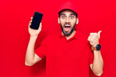 Sakallı, teslimat üniformalı, akıllı telefon tutan, ağzı açık gülümseyen genç yakışıklı bir adam. 