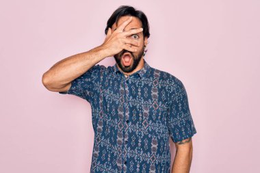 Yakışıklı İspanyol bohem bir adam pembe arka planda hippi tarzı giyinmiş. Şok olmuş bir şekilde yüzünü ve gözlerini kapıyor. Utanmış bir ifadeyle parmaklarının arasından bakıyor..