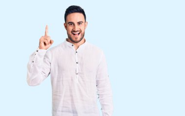 Gündelik giysiler giymiş genç yakışıklı bir adam başarılı bir fikri işaret ediyor. Heyecanlı ve mutlu. Bir numara.. 