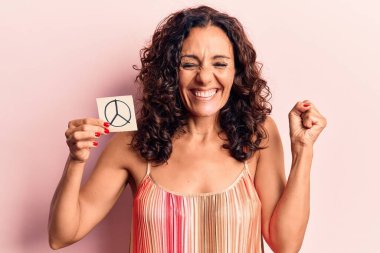 Middle age beautiful woman holding peace symbol reminder screaming proud, celebrating victory and success very excited with raised arm  clipart
