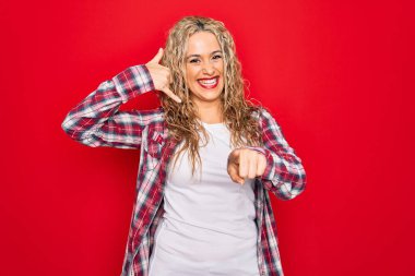 İzole edilmiş kırmızı arka planda dikilen ve gülümseyen genç, sarışın bir kadın telefon jestinde konuşarak seni işaret ediyor. Ara beni..