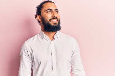 Gündelik giysiler giyen genç bir Arap yüzü gülücükle yan yana bakıyor, doğal bir ifade. Kendinden emin gülen. 