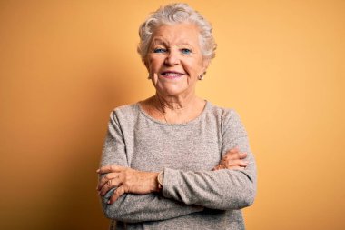 Son sınıf güzeli, günlük tişört giyen, izole edilmiş sarı arka planda duran mutlu yüzlü, kollarını kavuşturup kameraya bakan bir kadın. Pozitif kişi.