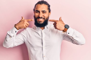 Gündelik giysiler giyen genç bir Arap neşeli bir şekilde gülümseyip parmaklarıyla ve ağzıyla işaret ediyor. diş sağlığı kavramı. 