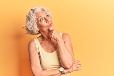 Kıdemli, gri saçlı, sıradan kıyafetler giyen, bir soru hakkında endişeli ve gergin bir kadın. 