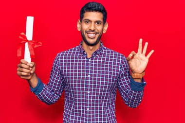 Diploma almış genç Latin bir adam parmaklarıyla imza atıyor, gülümsüyor ve mükemmel bir sembol oluşturuyor. 