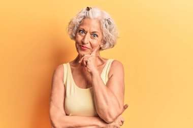 Üstün gri saçlı, günlük kıyafetler giyen, kameraya kendinden emin, kolları çapraz ve çenesi açık gülümseyen bir kadın. Olumlu düşünmek. 