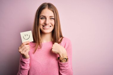 Genç, güzel, kızıl saçlı kadın elinde gülümseyen emoji mesajıyla hatırlatma kâğıdı tutuyor.