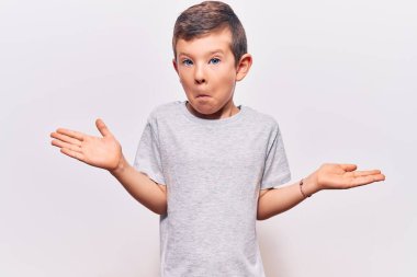 Sıradan kıyafetler giyen sevimli sarışın çocuk, elleri ve kolları havada, kafası karışmış bir ifade. şüphe kavramı. 