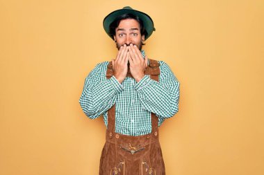 Almanya festivali için geleneksel Alman Ekim Festivali kıyafeti giyen genç yakışıklı adam gülüyor ve utanıyor. Ağzı ellerle, dedikoduyla ve skandal konseptiyle örtüyor.