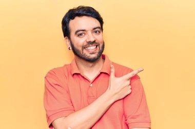 Gündelik giysiler giyen genç İspanyol adam gülümseyen, eli ve parmağı yana doğru gösteren. 