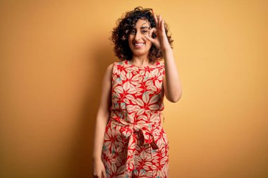 Genç, güzel, kıvırcık Arap kadın tatilde. Çiçekli bir elbise ve güneş gözlüğü takıyor. Gülümsüyor. Başarılı ifade.