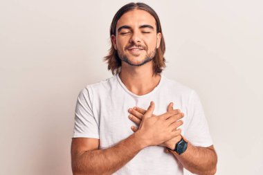 Sıradan kıyafetler giyen, elleri göğsünde, gözleri kapalı gülümseyen ve yüzünde minnet ifadesi olan genç yakışıklı bir adam. sağlık kavramı. 