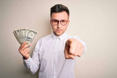 Genç beyaz iş adamı elinde bir dolarlık banknotlarla kamerayı işaret ediyor ve sen, el işareti, ön taraftan pozitif ve kendinden emin bir hareket.